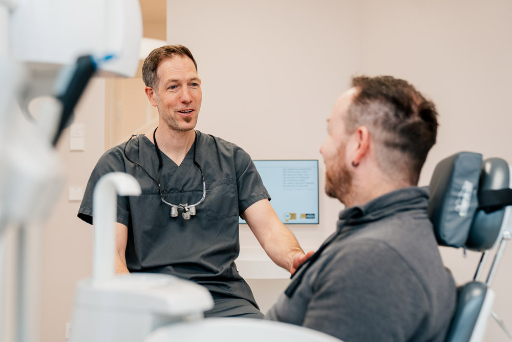 Dr. Phillip Wallowy bespricht Behandlung mit Patienten im Behandlungsstuhl